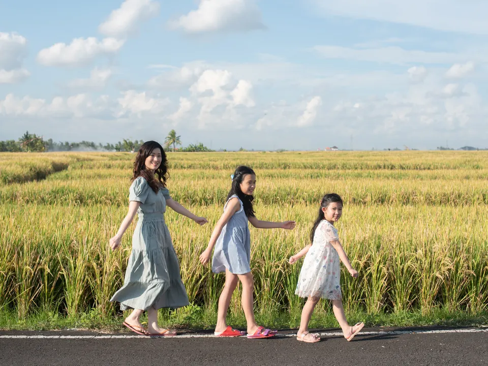 Mother and daughters walking beside green rice fields