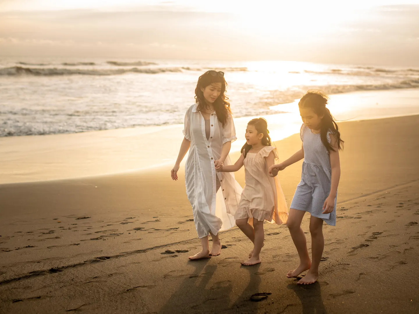Mother and daughters holding hands on a sunlit Bali beach